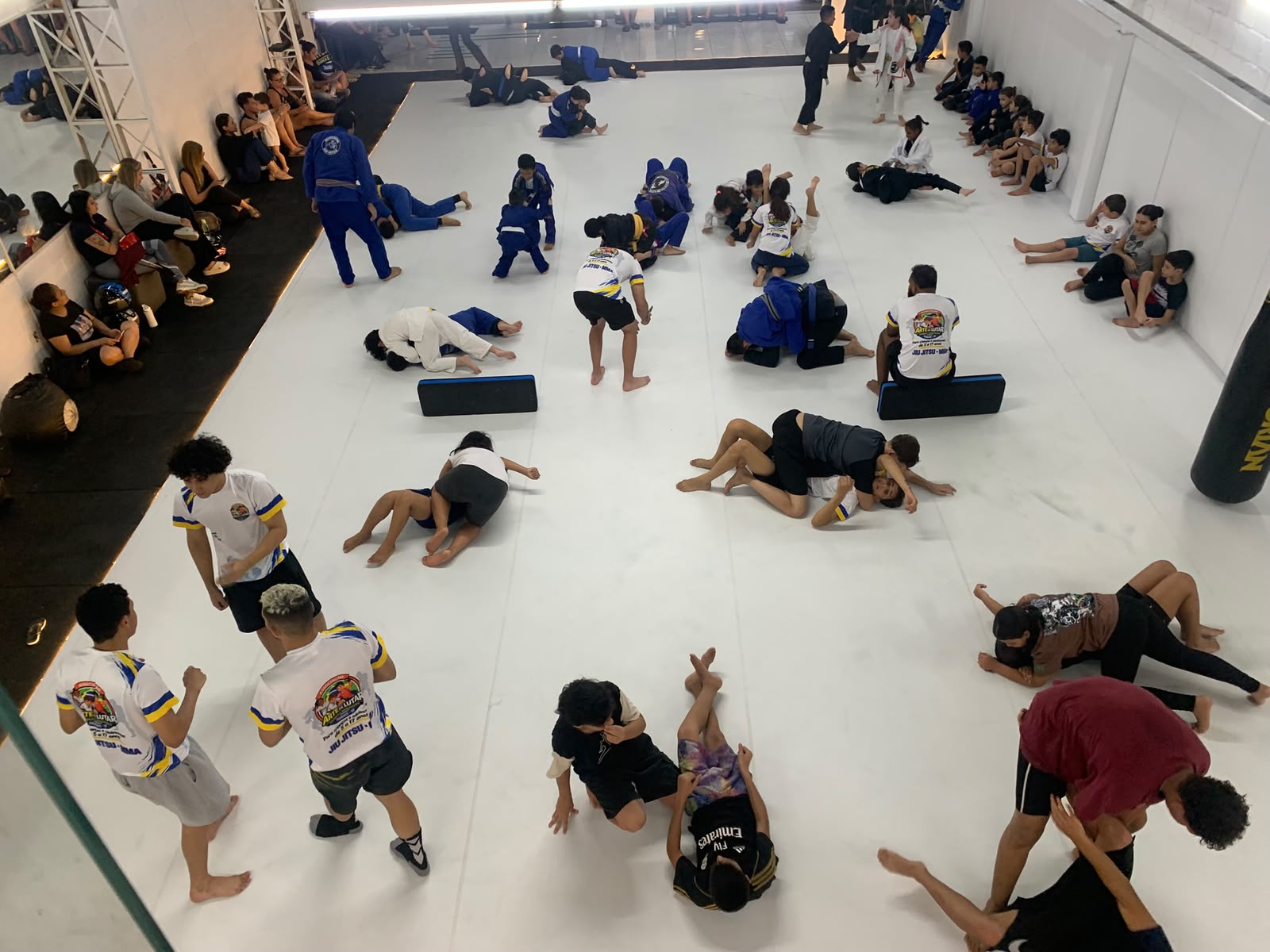 Crianças e adolescentes treinando Jiu-Jitsu no tatame da associação, vistos do alto