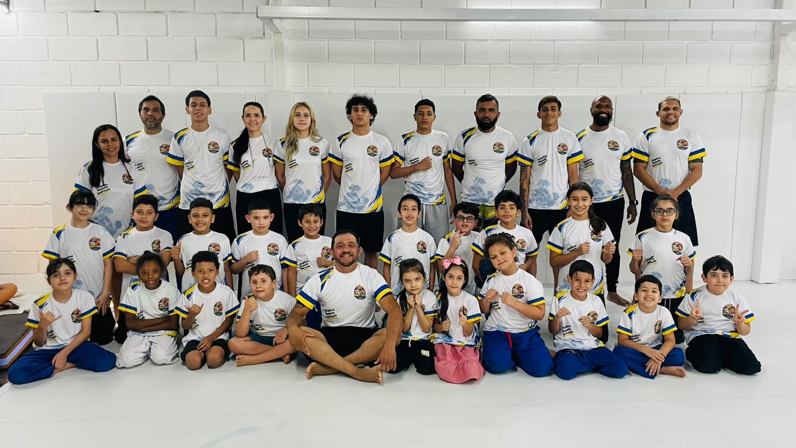 Alunos, professores e equipe da Associação Arte de Lutar reunidos no tatame, com a camiseta do projeto